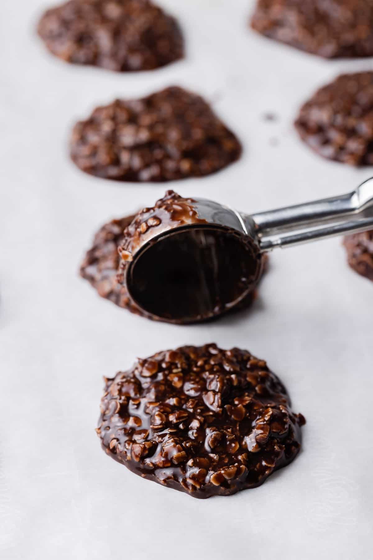 Sooping no bake chocolate oatmeal cookies onto baking sheet.