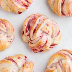Six cranberry orange sweet rolls on a baking sheet lined with parchment paper.
