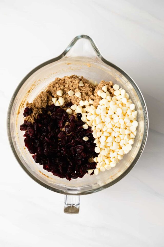 Dried cranberries and white chocolate chips being mixed into oatmeal cookie dough