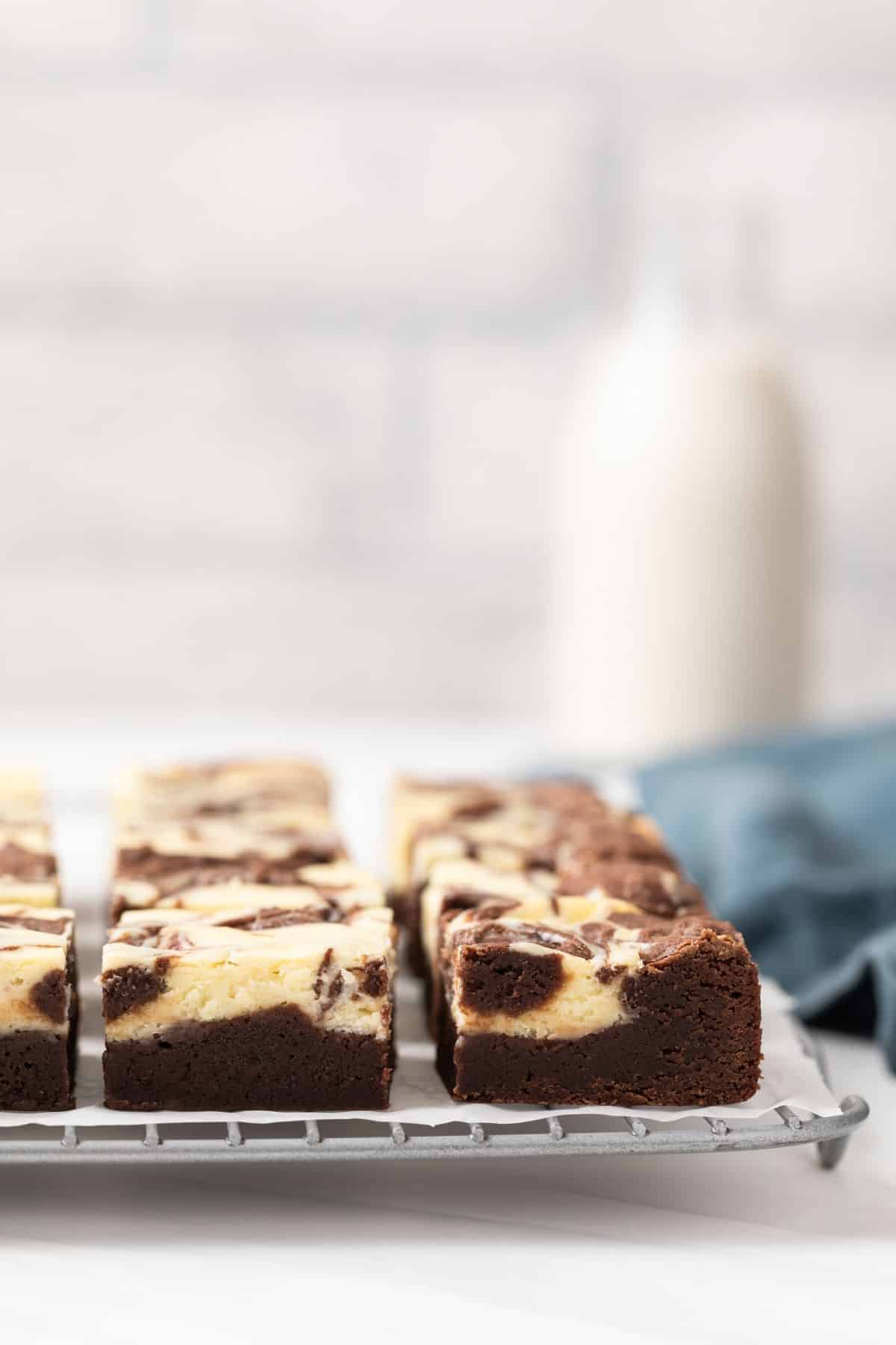 Cream cheese brownies on a wire rack with a glass jar of milk.