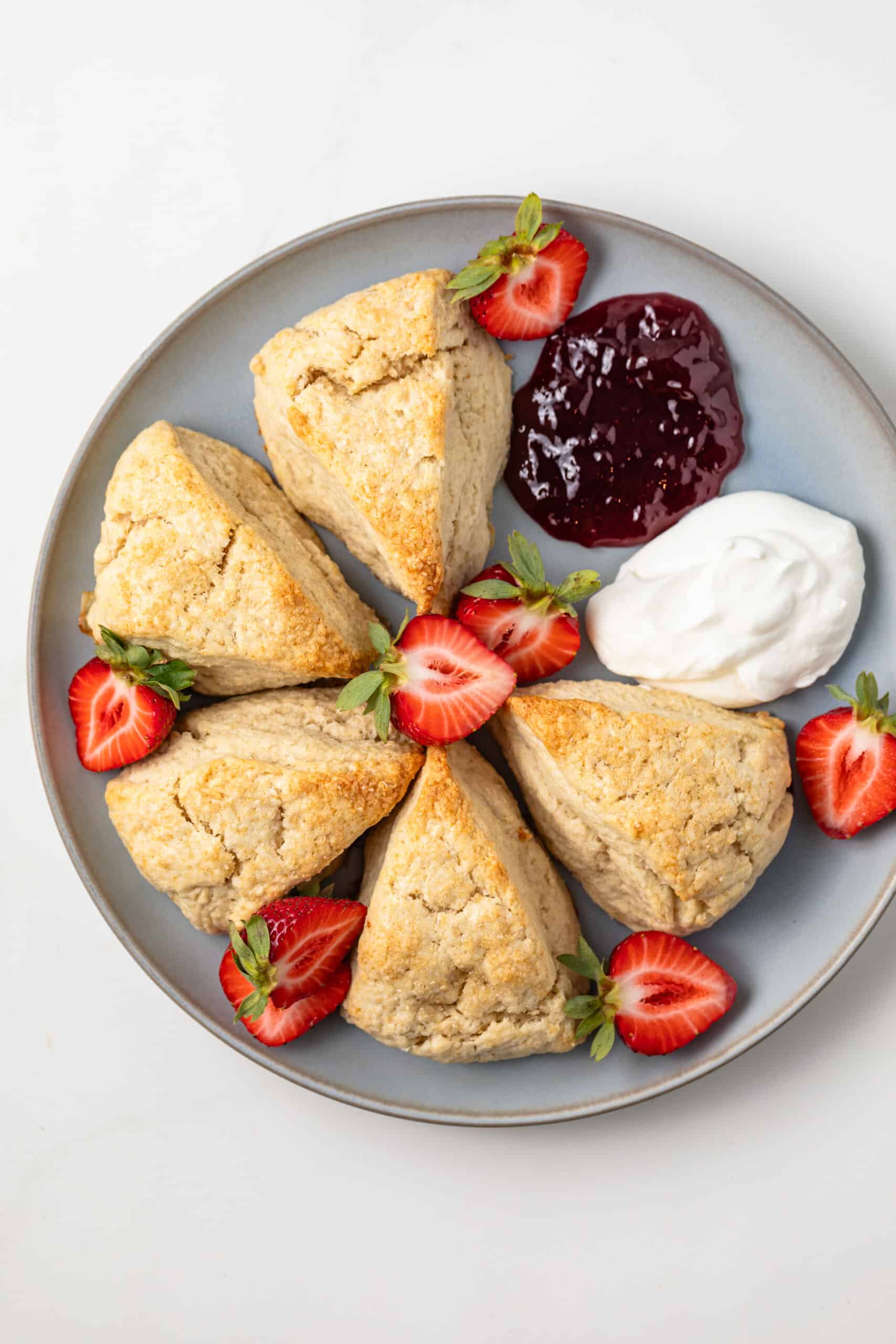 Plate of cream scones with strawberries, jam, and whipped cream.
