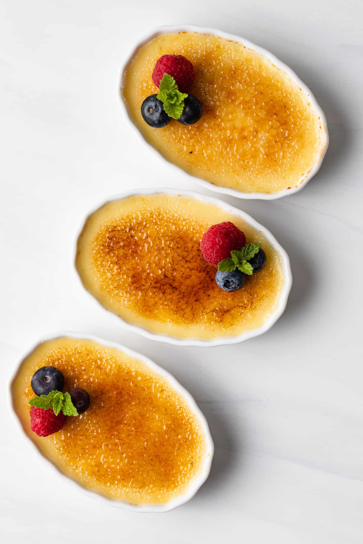 overhead of three ramekins with creme brulee and fresh berries