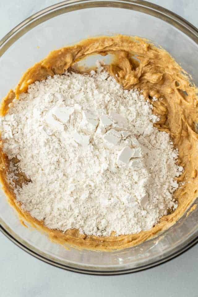 Flour added to wet ingredients in a glass bowl.