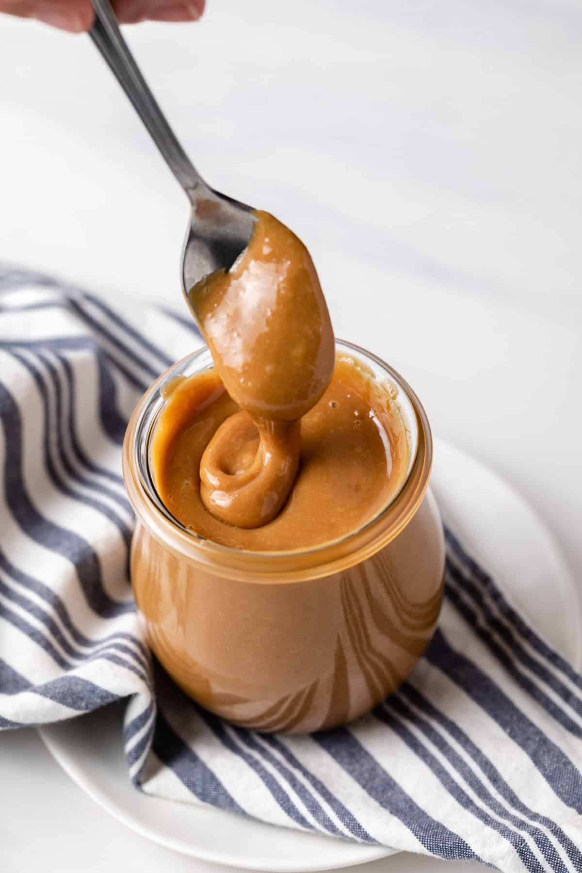 a spoon drizzling dulce de leche into a glass jar