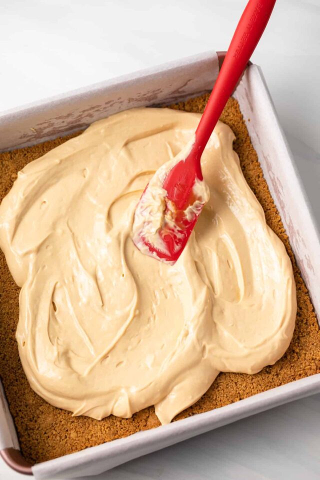Cheesecake layer being spread onto graham cracker crust