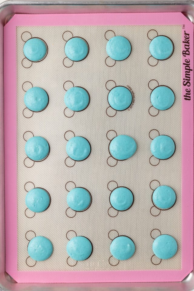 Piped macarons on baking sheet with silicone mat.