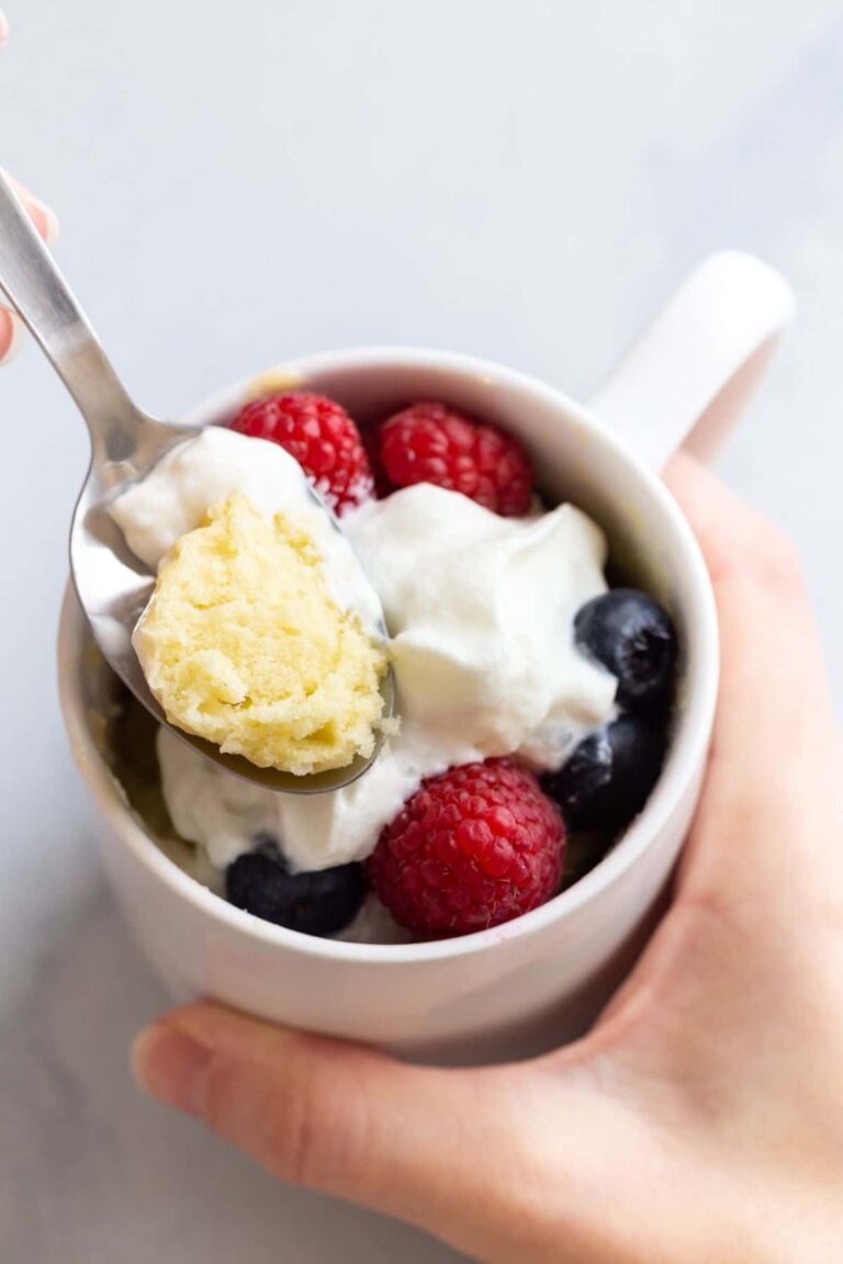 A spoon taking a bite out of vanilla cake in a mug.