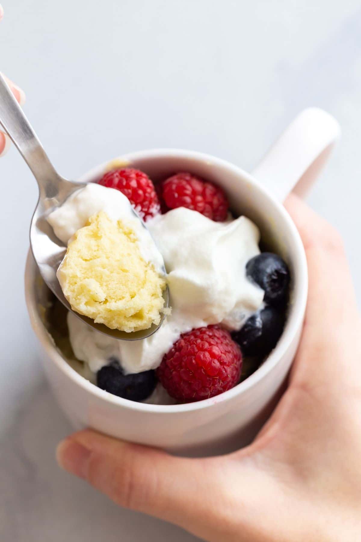 A spoon taking a bite out of vanilla cake in a mug.