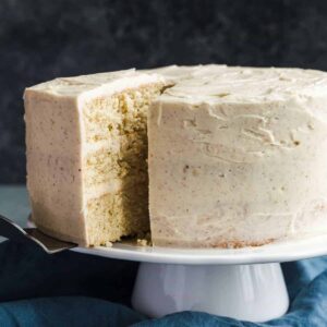 Eggnog cake on a white cake stand with a slice being taken out.