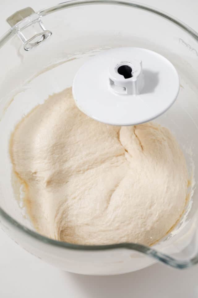 Focaccia dough in glass bowl with dough hook.