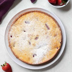 over head view of fresh strawberry cake on white plate with whole strawberries scattered around