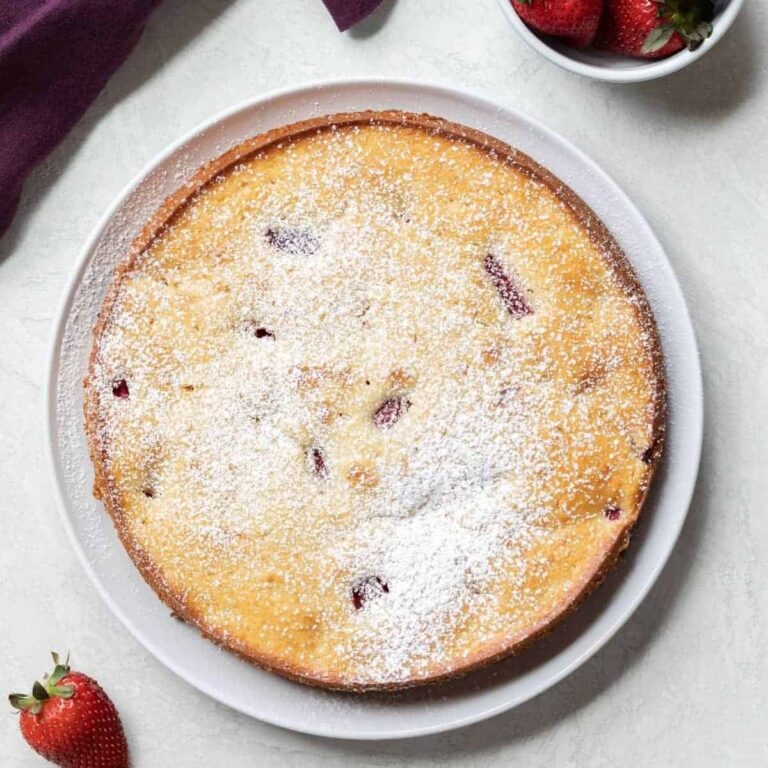 over head view of fresh strawberry cake on white plate with whole strawberries scattered around