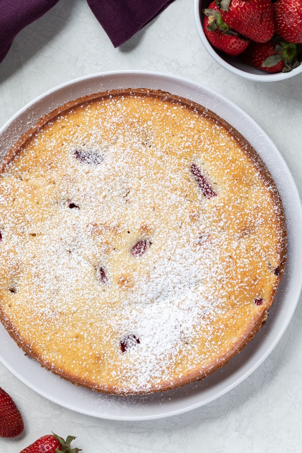over head view of fresh strawberry cake on white plate with whole strawberries scattered around