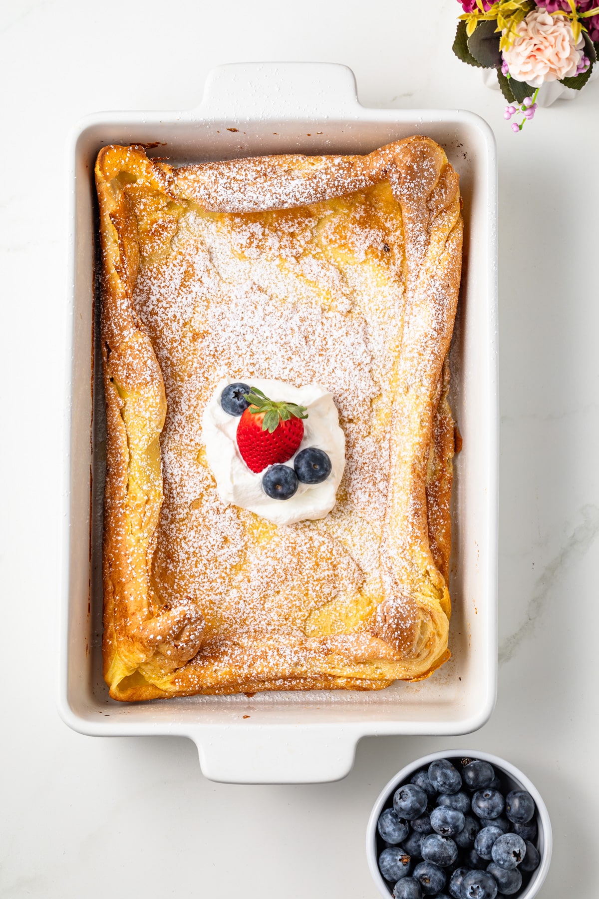 German pancake dusted with powdered sugar and whipped cream.