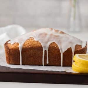 Side view of glazed lemon bread on wood board.