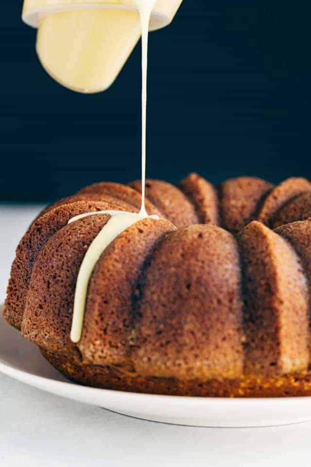 Glaze being poured over a pumpkin bundt cake sitting on a cream colored plate.