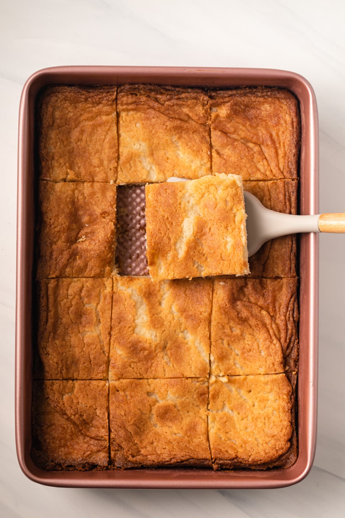 Gooey butter cake in cake pan with spatula taking a slice out.