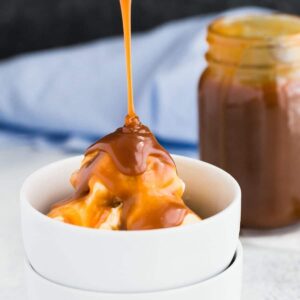Homemade caramel sauce bring drizzled over a scoop of ice cream in a white bowl.