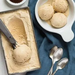 Homemade coffee ice cream being scooped out of a loaf pan into a white bowl.