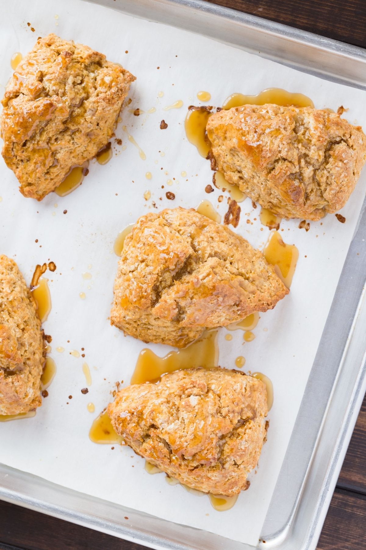 Baked sweet potato scones drizzled in honey citrus glaze on a baking sheet lined with white parchment paper.