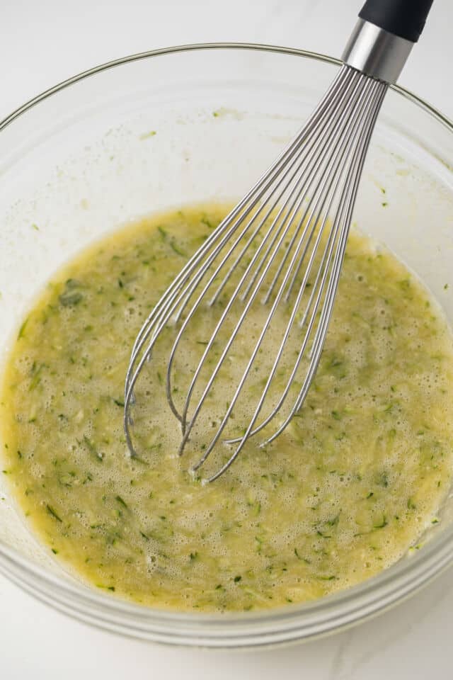 Wet ingredients with zucchini combined in glass bowl.