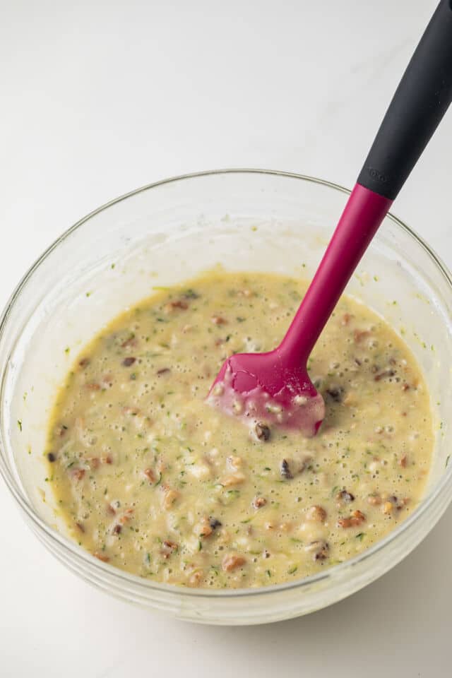 Zucchini bread batter in glass bowl with spatula.