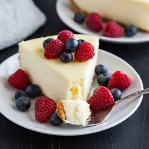 A slice of cheesecake topped with fresh berries and a fork taking out a bite.