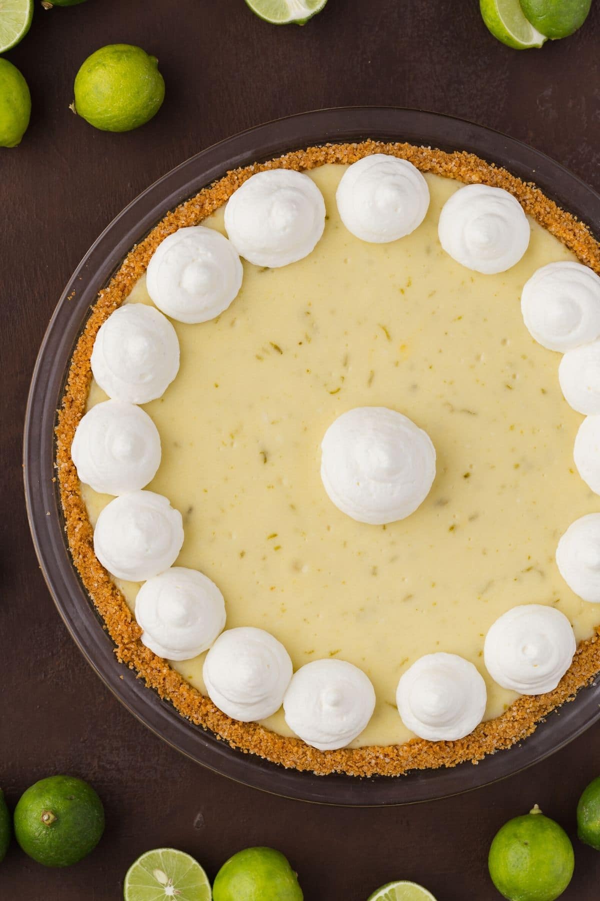Close overhead view of a whole key lime cheesecake pie with swirls of whipped cream on top.