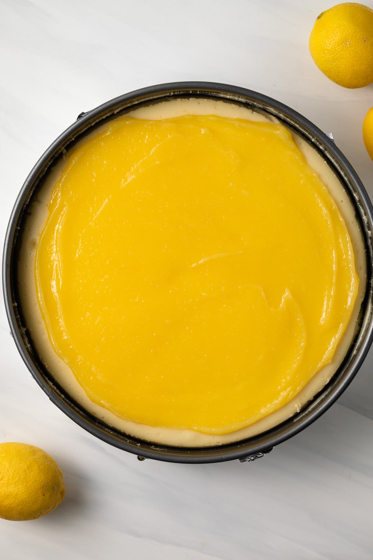 Lemon curd over lemon cheesecake in pan.