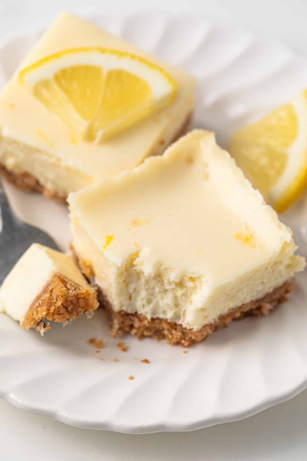Lemon cheesecake bar on a plate with a fork taking a bite out.