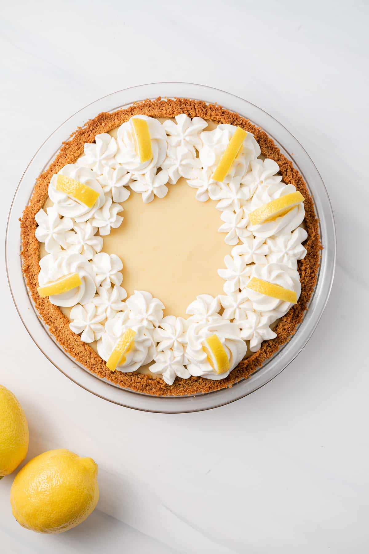 Overhead of lemon pie topped with whipped cream and lemon wedges.