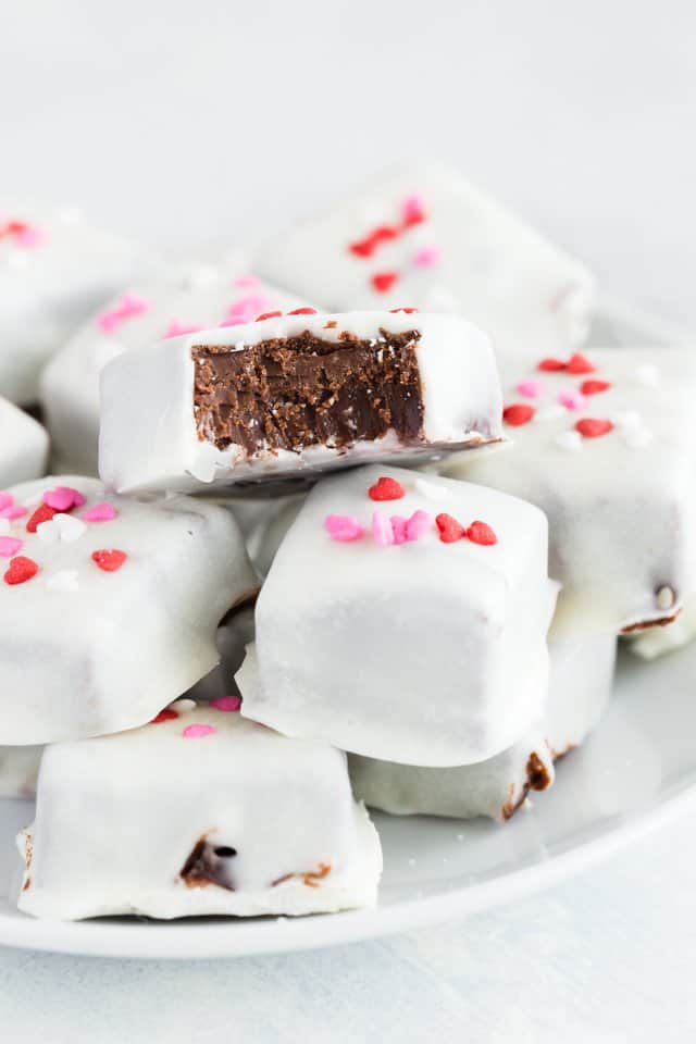 Mexican Hot Chocolate Fudge stacked on a white plate with a bite out of one piece so the inside is visible.