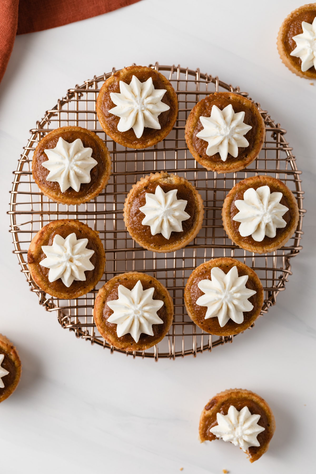 overhead of mini pumpkin pies with whipped cream set on a round wire rack