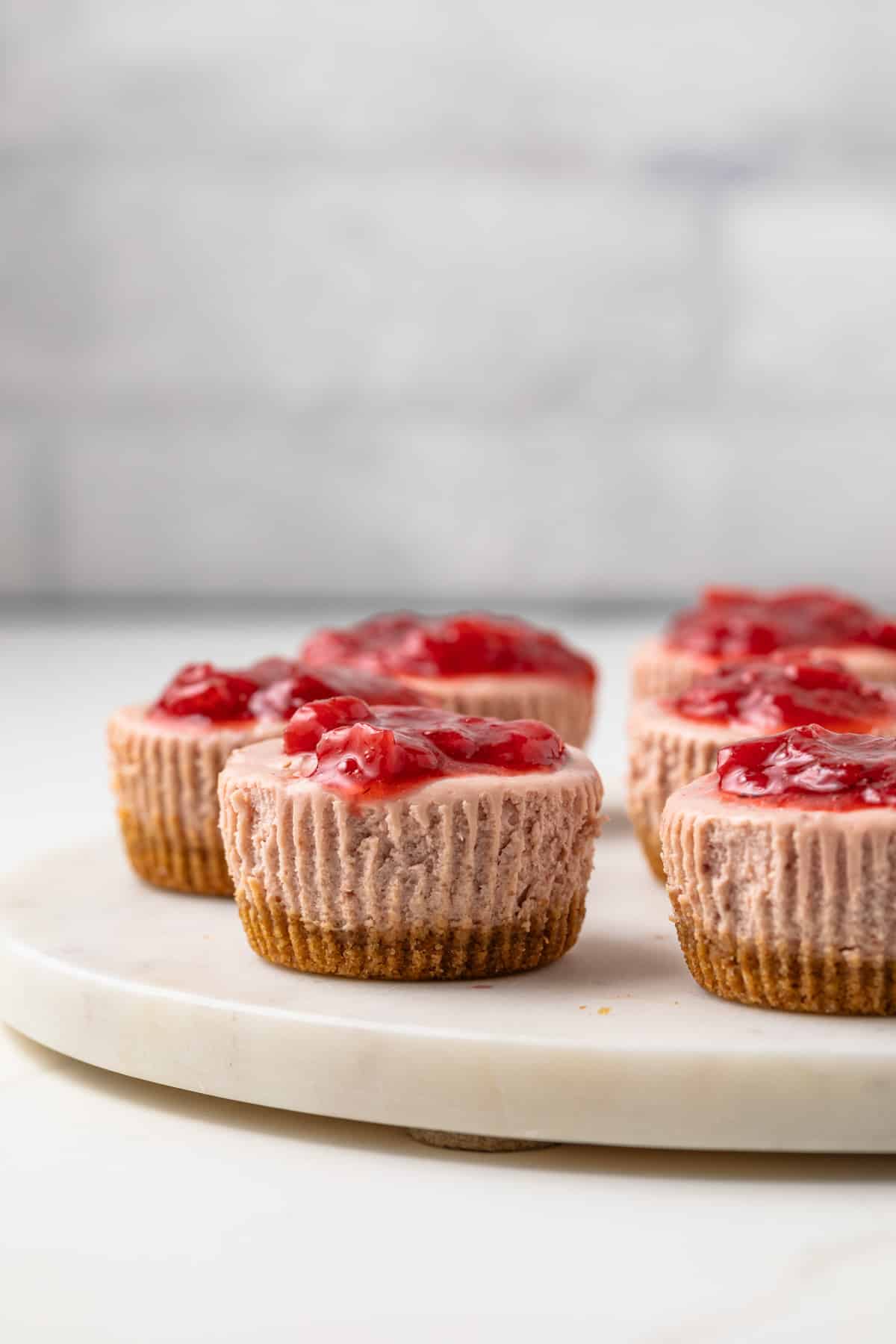 Side view of mini strawberry cheesecakes on serving platter.