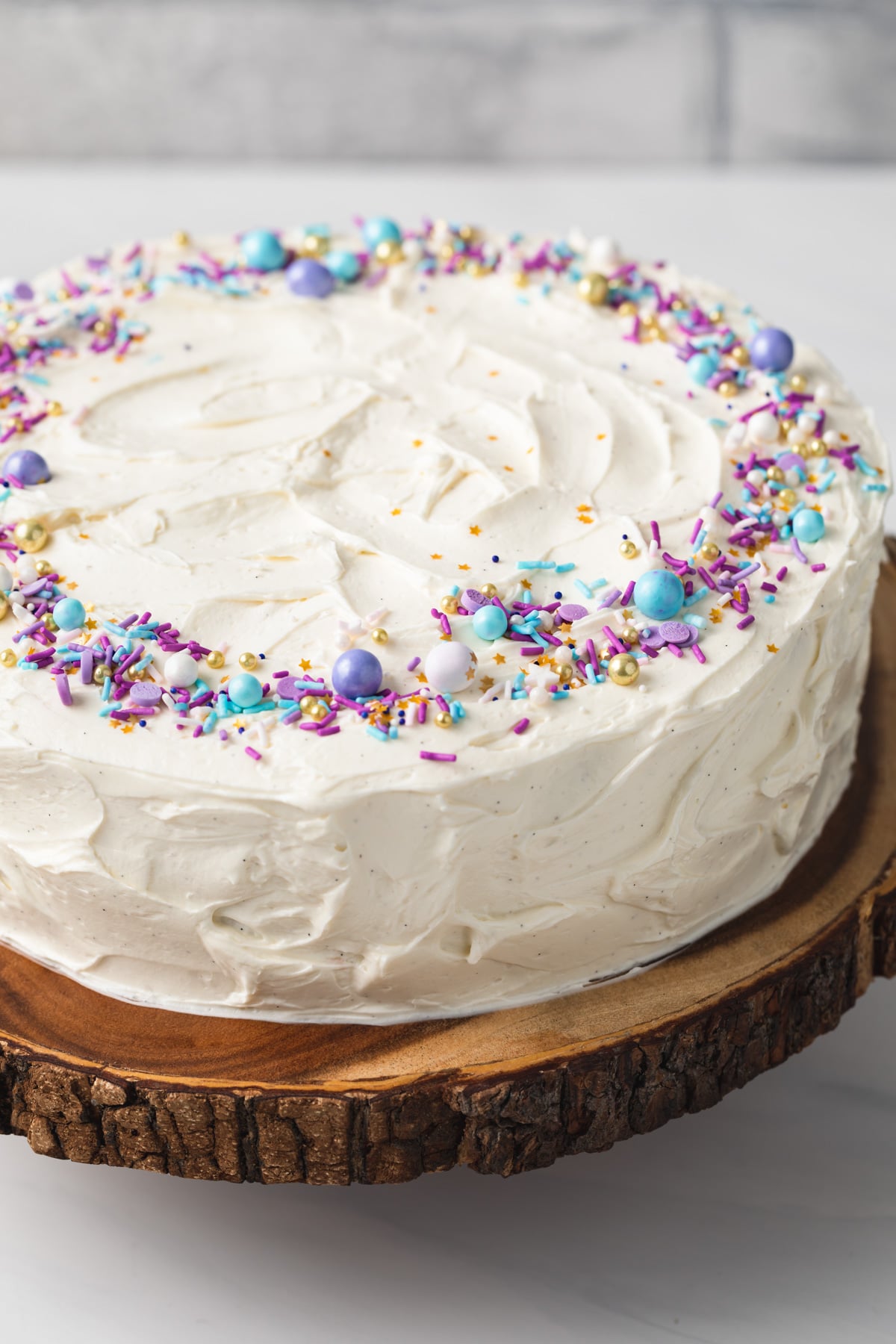 angled view of vanilla cake with colorful sprinkles on a wooden cake stand