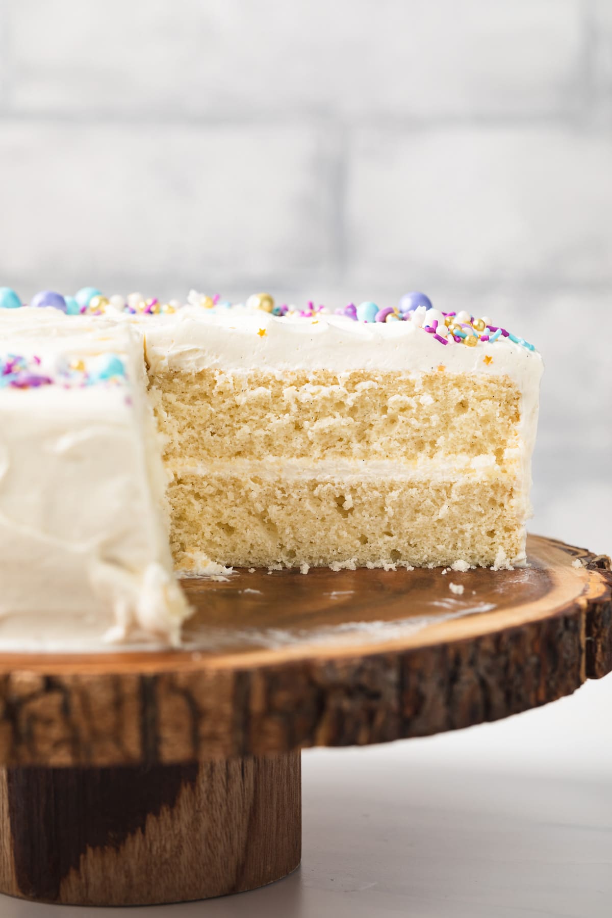 side view of a moist vanilla cake on wooded cake stand with a slice cut out