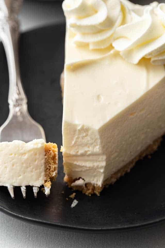 slice of no bake cheesecake on a white plate with a fork taking a bite out