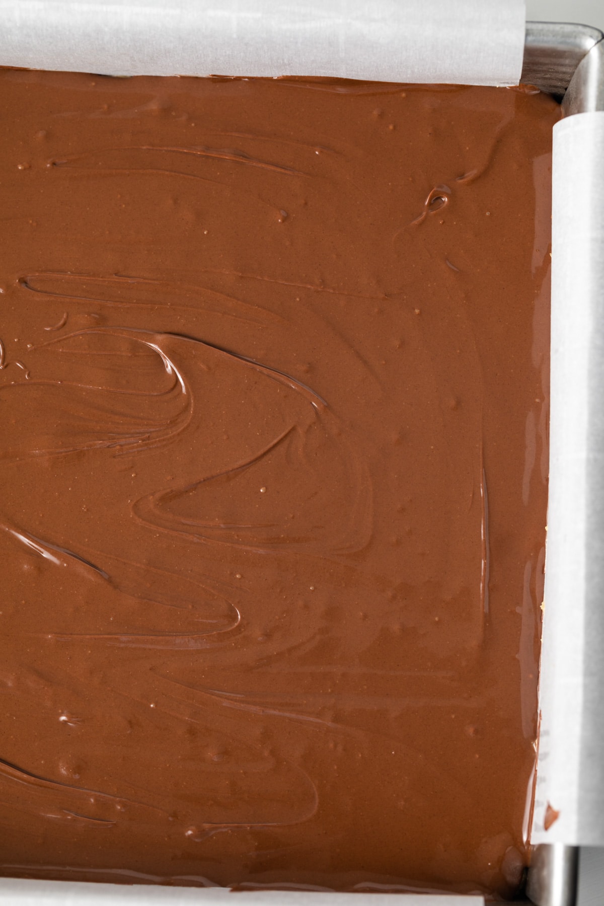 Melted chocolate over peanut butter in pan.
