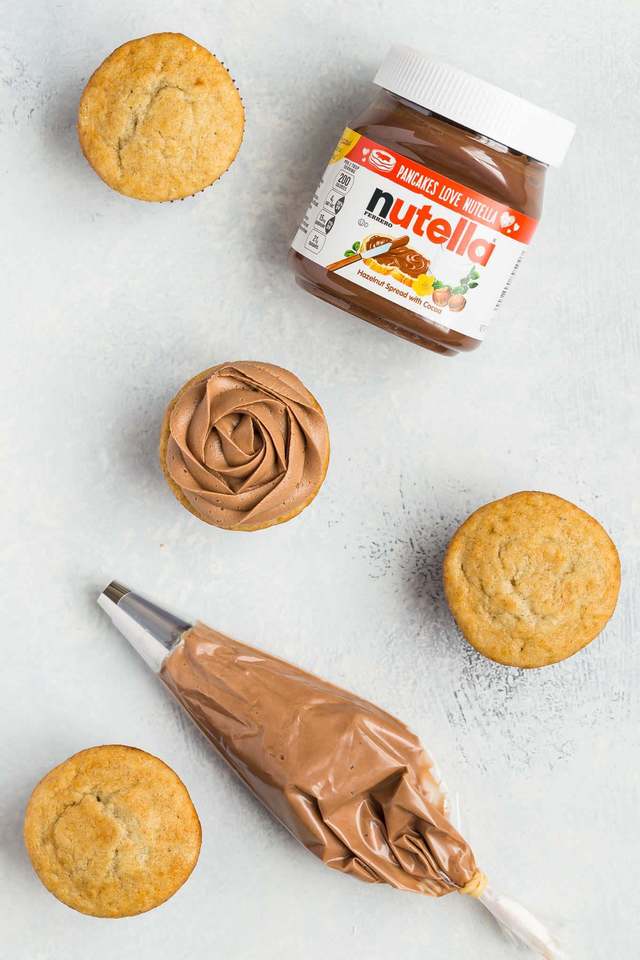 Buttercream frosting with Nutella and cupcakes scattered on a white surface.