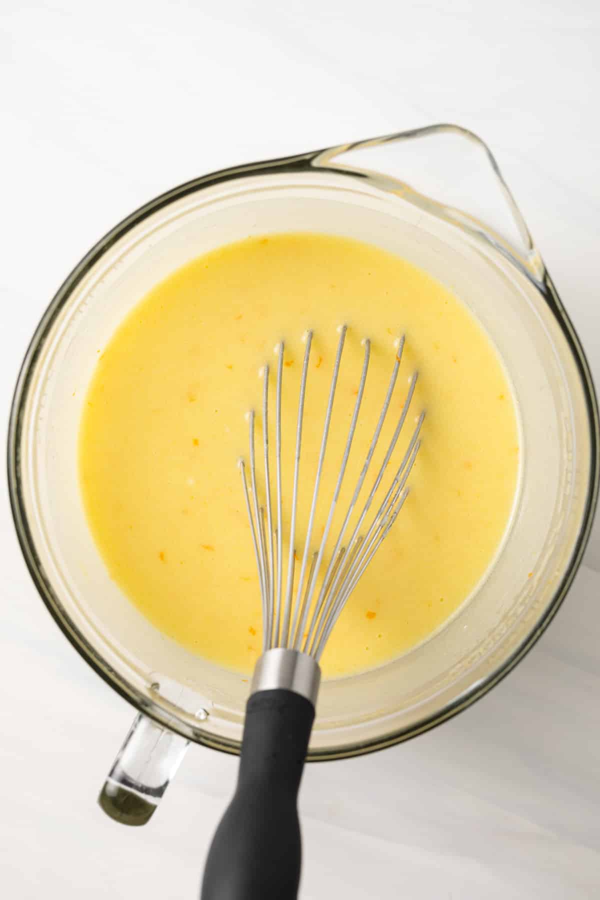 Wet ingredients for olive oil cake whisked in a glass bowl.