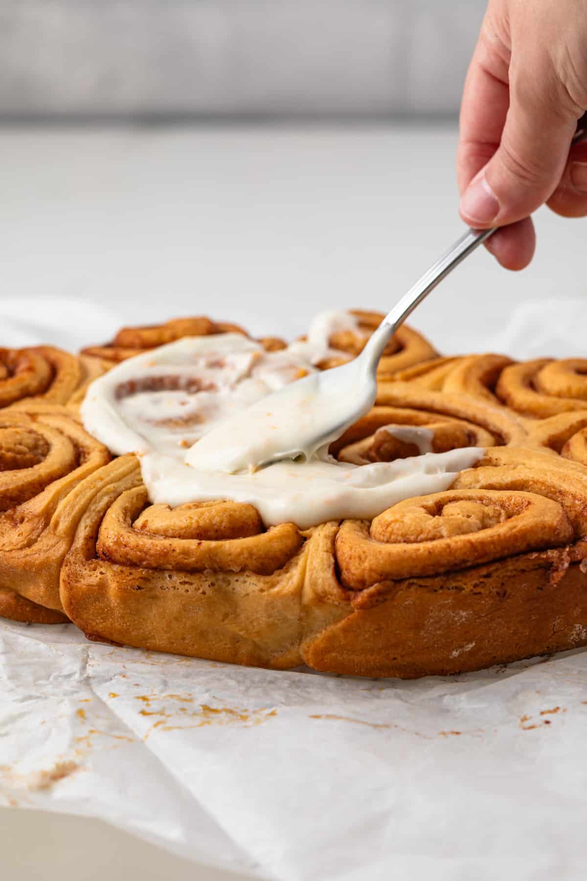Icing being spread over orange sweet rolls.