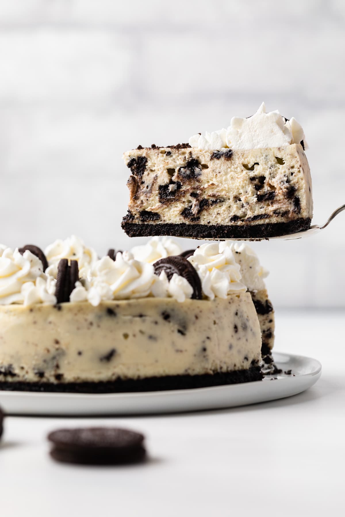 side view of slice of oreo cheesecake being taken out and held above whole cheesecake