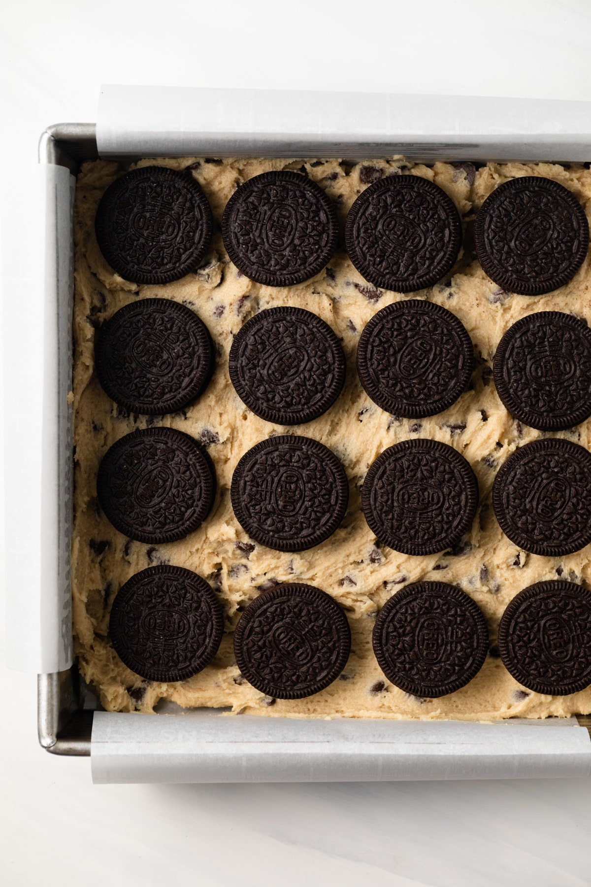 Oreos over cookie dough in baking pan.