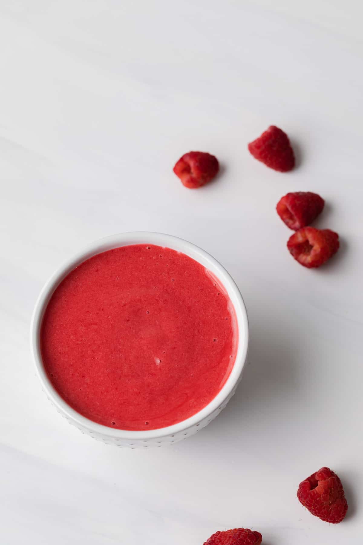 raspberry sauce in a white bowl with fresh raspberries scattered around