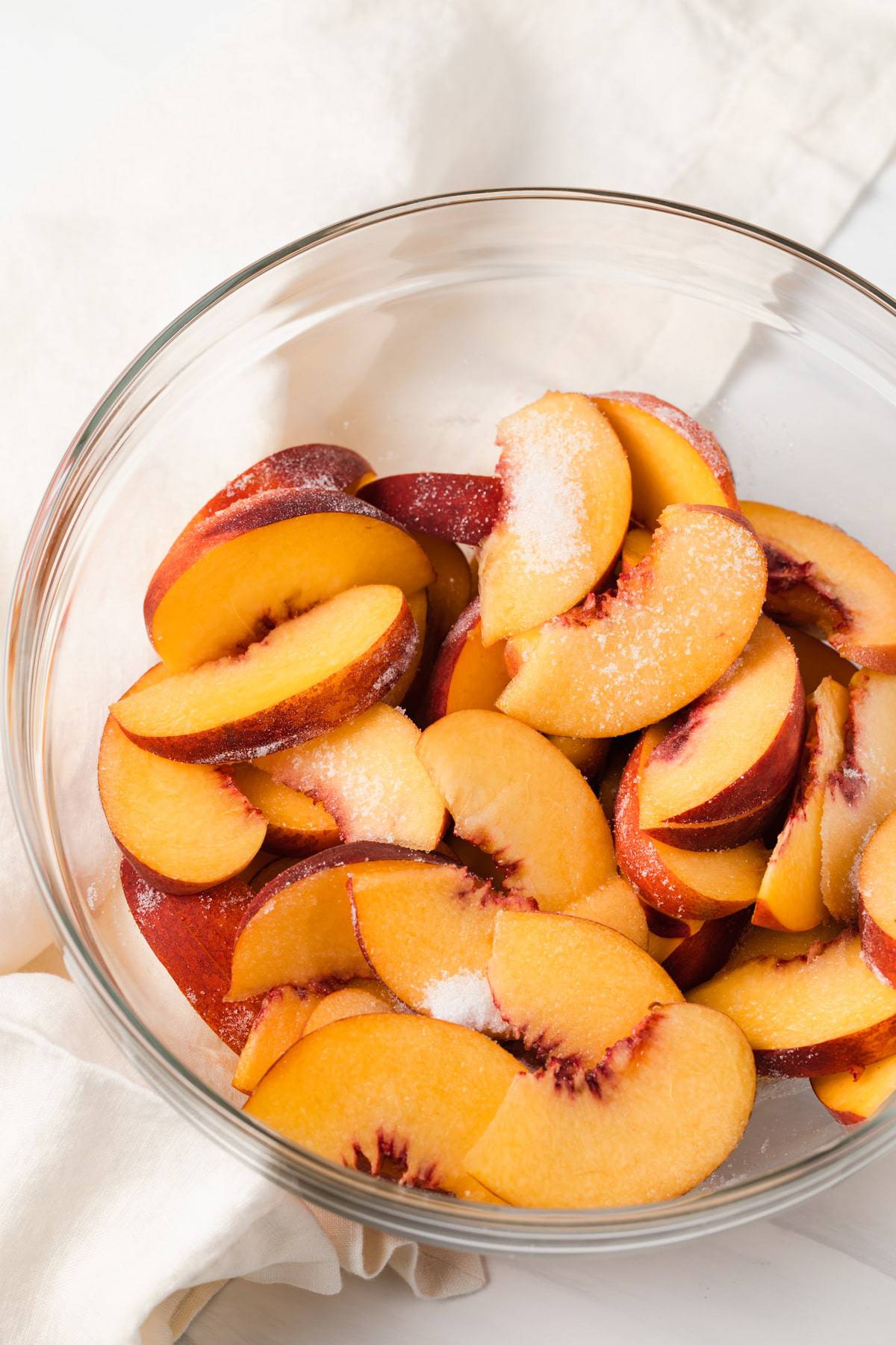 glass bowl filled with peaches tossed in sugar