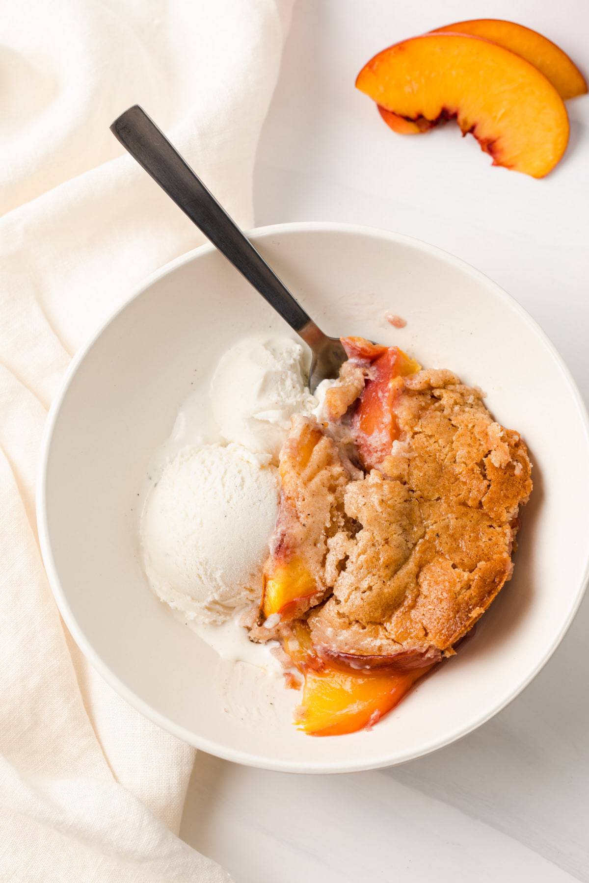 closeup of peach cobbler with vanilla ice cream in white bowl with a spoon