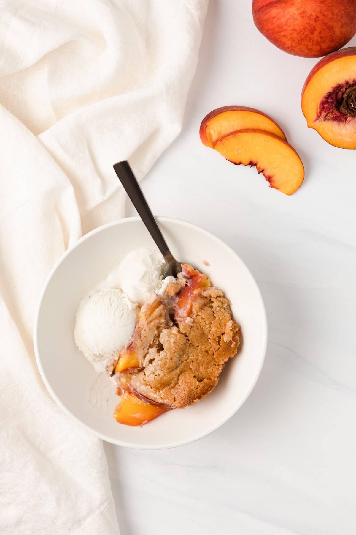 overhead of peach cobbler with vanilla ice cream in white bowl