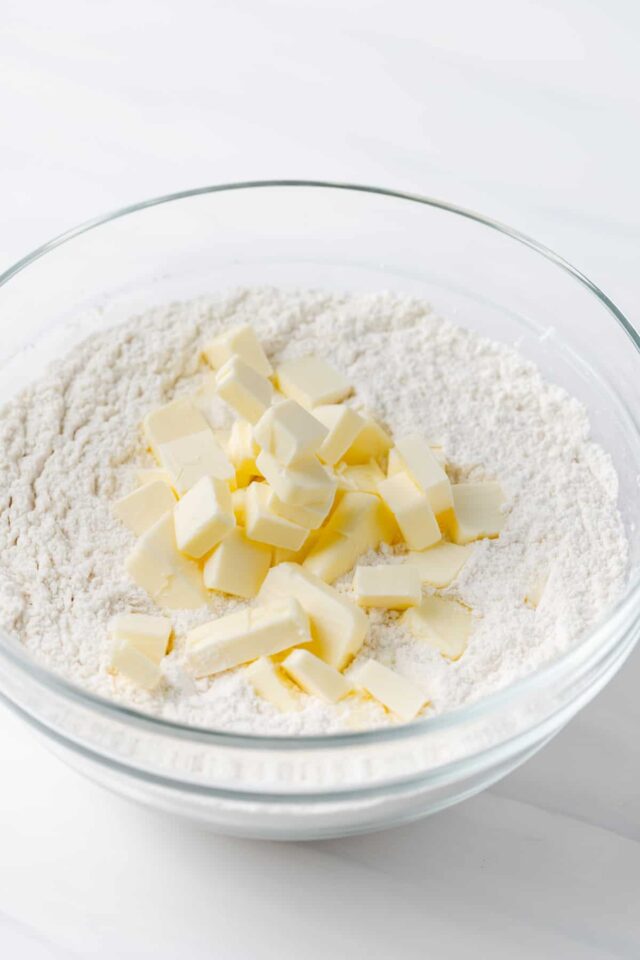 Chunks of cold butter on top of flour in a white bowl