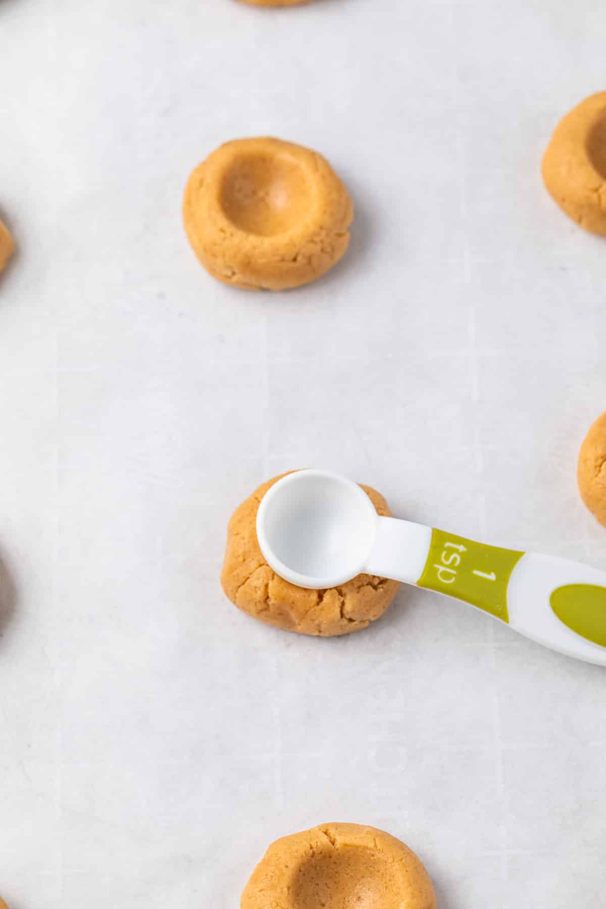 Teaspoon making an indentation in cookie dough balls.