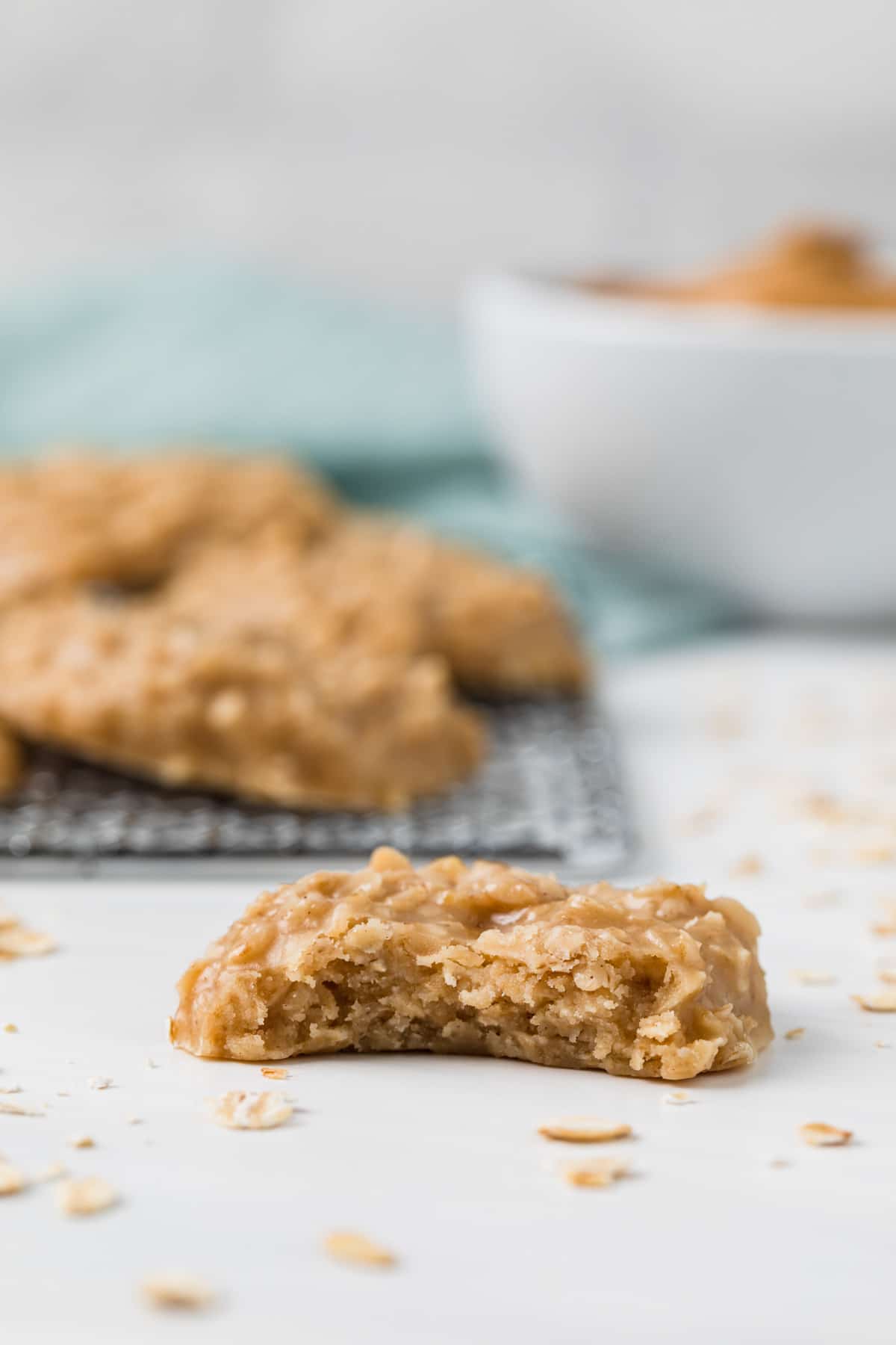 front view of a peanut butter no bake cookies with bite taken out sitting in front of cookies on a wire rack and bowl of peanut butter